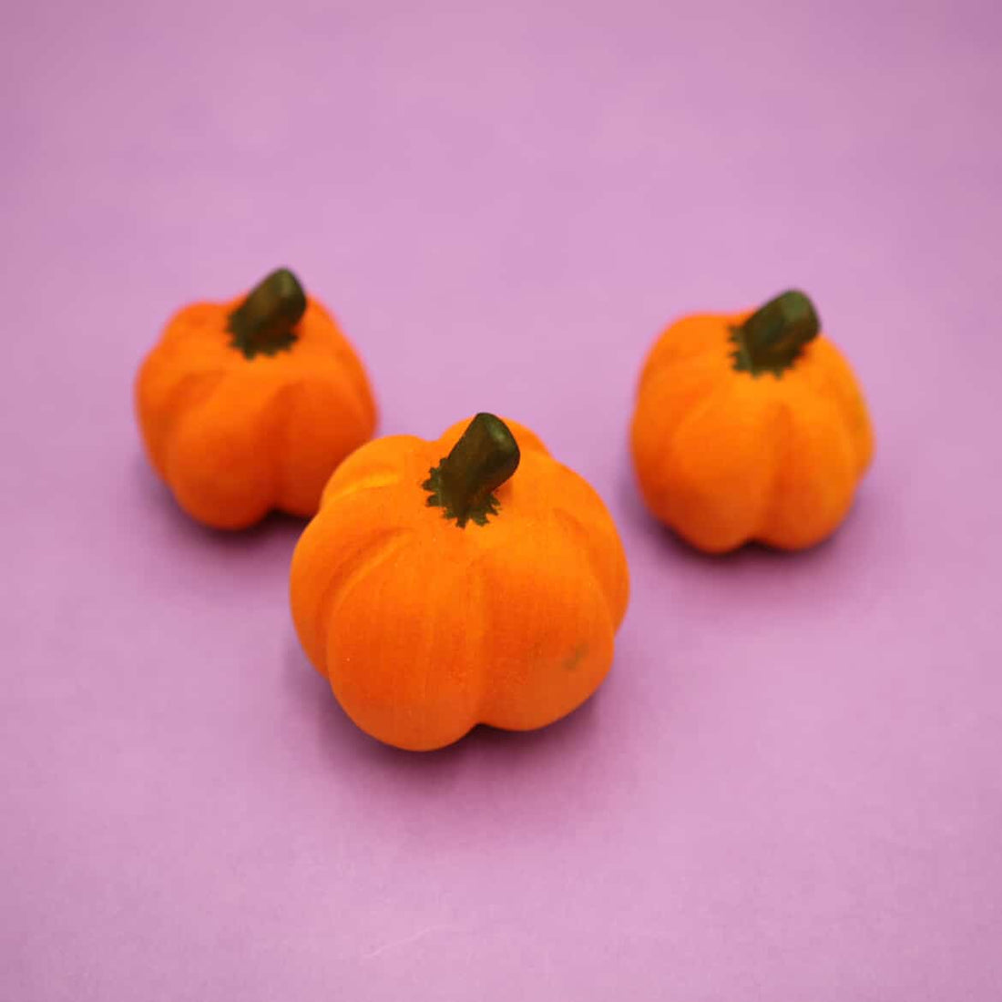 Three plain wooden pumpkins with carved ribs and dark stems