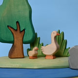 Wooden gosling beside larger geese in a small-world pond scene · view 3