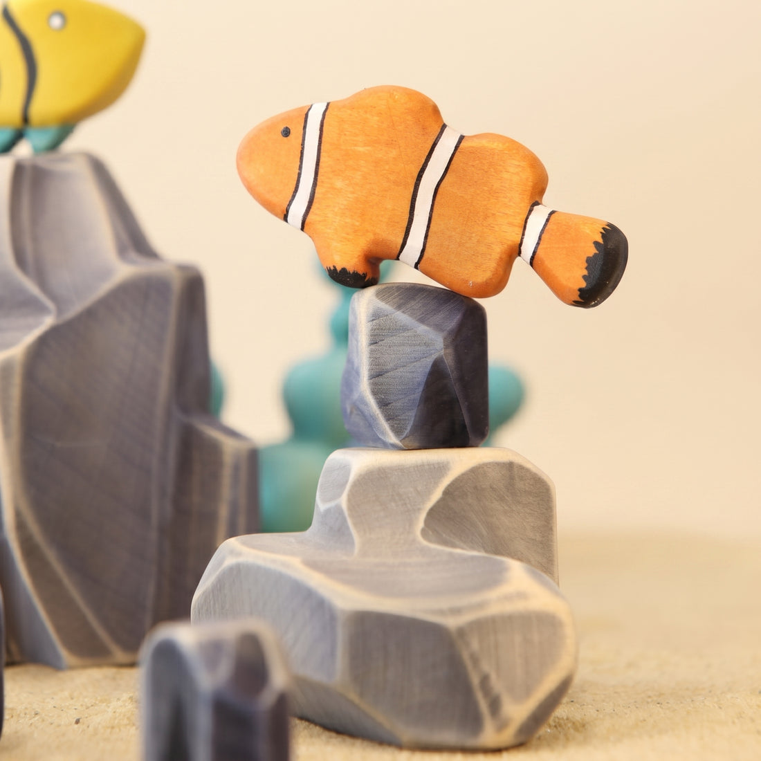 Wooden clown fish painted orange with white bands, beside a pale rock