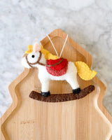 Felt Christmas rocking horse ornament with a golden mane, red saddle, and brown rocker, hanging from a white loop · view 1
