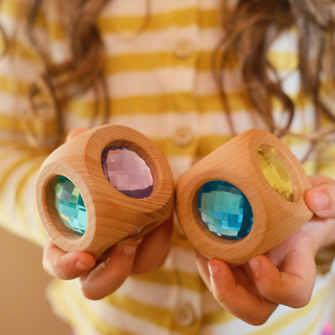 A child holding two Bauspiel Magic Cube Pastel wooden cubes with pastel gems